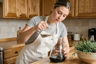 Femme versant un liquide d'un verre doseur de 10 cl dans une carafe graduée en litre sur un comptoir en bois